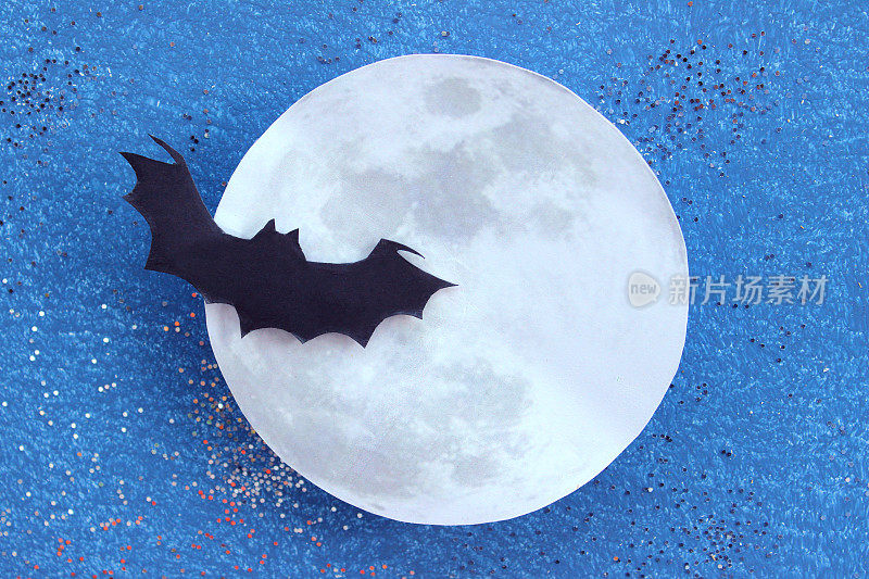 黑色蝙蝠的剪影在纸月亮前飞行，万圣节村庄/万圣节的背景